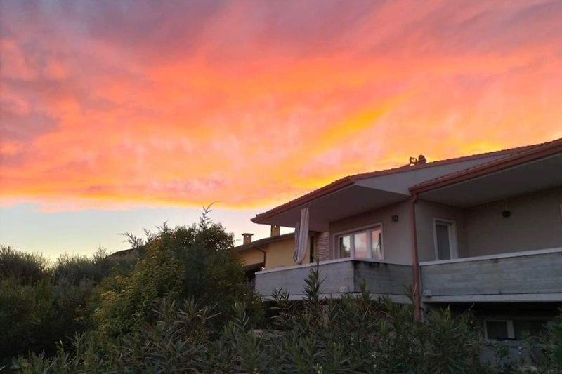 Casa rurale al tramonto con cielo rosso.