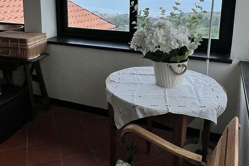 Fenster mit Blumenvase, Holztisch und Stuhl.