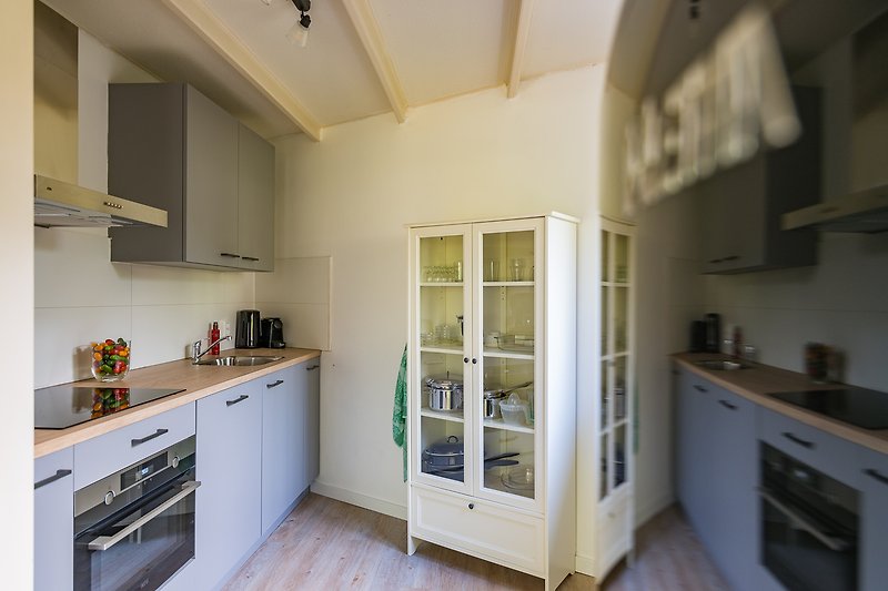 Open keuken met inbouwapparatuur, servies, pannen en een design koelviescombinatie.