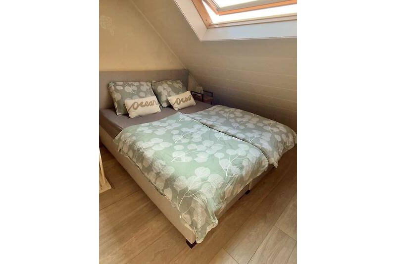 Gemütliches Schlafzimmer mit Holzbett, Fenster und gemusterten Bettwäsche.