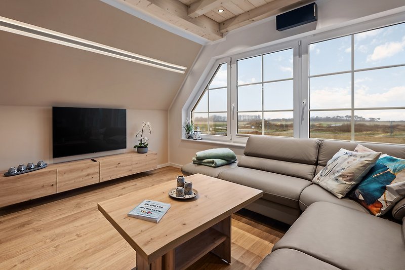 Gemütliches Wohnzimmer mit bequemer Couch, Holzboden und großem Panoramafenster mit Meerblick. FeWo Ostseeblick