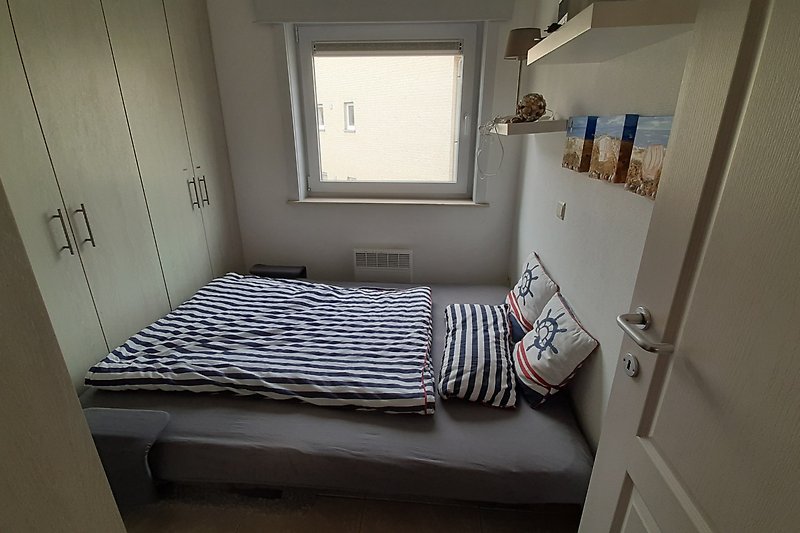 Gemütliches Schlafzimmer mit Holzbett, gemütlicher Bettwäsche und Fenster.