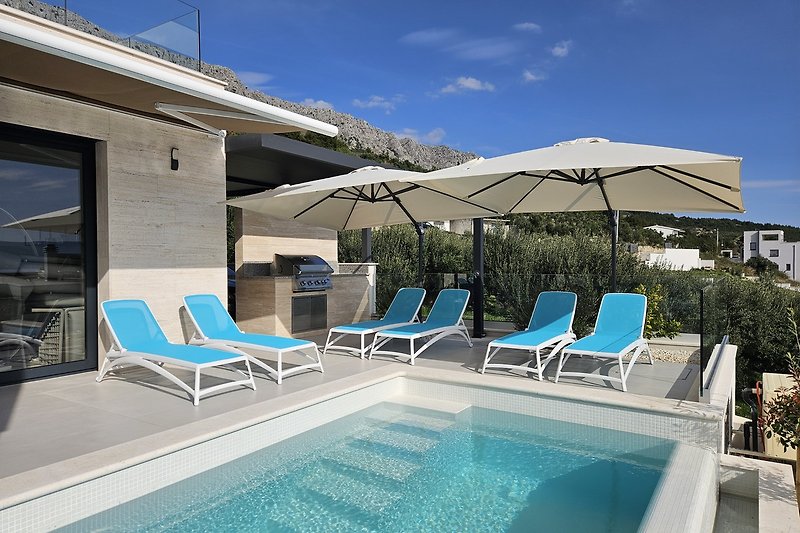 Luxuriöser Poolbereich mit Sonnenliegen, Schirmen und tropischer Umgebung.