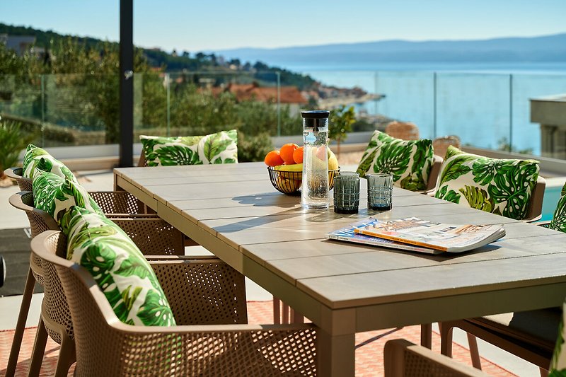 Einladende Terrasse mit grünem Garten, stilvollen Möbeln und Blick auf das Wasser.