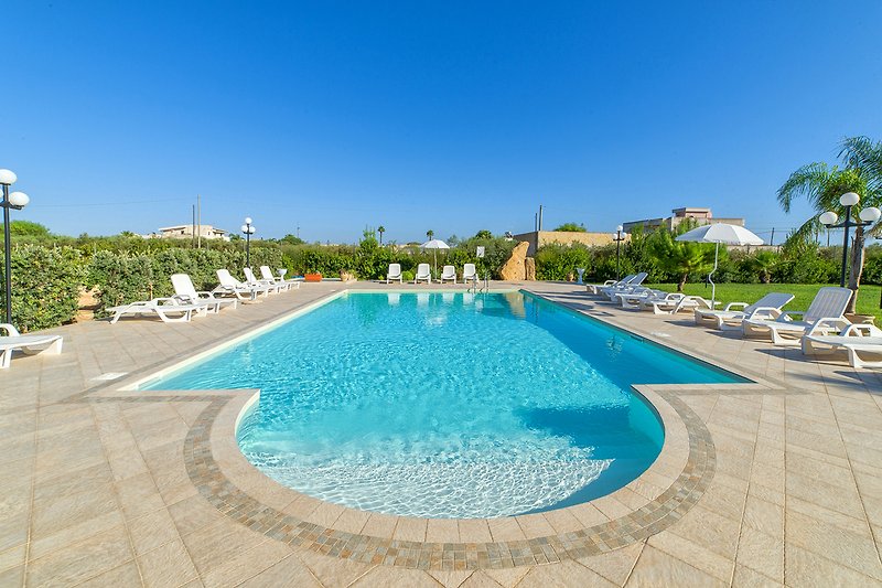 Una piscina azzurra circondata da piante, con mobili da esterno per il relax.