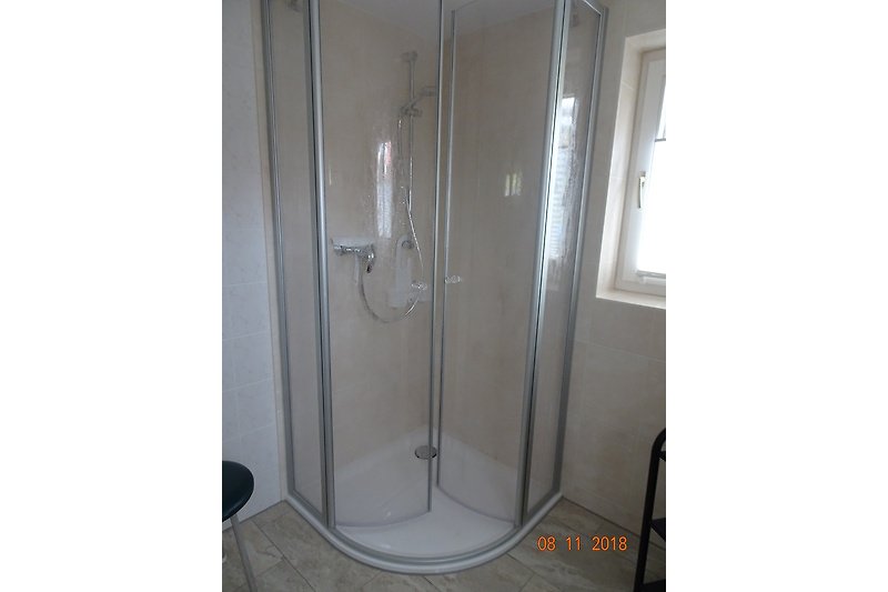 Moderne Badezimmerausstattung mit transparenter Duschtür und Nickelarmaturen.