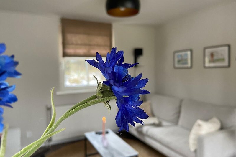 Gemütliches Wohnzimmer mit blauen und violetten Blumen auf dem Tisch.