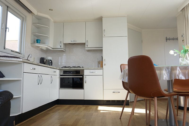 Moderne Küche mit Holzmöbeln, Fensterfront, Küchengeräten und Stühlen.