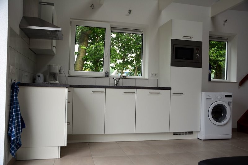 Mooie keuken met wasruimte, kasten en raam.