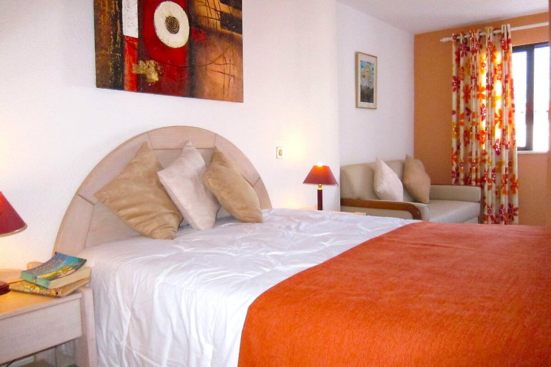 Stylish bedroom with cozy bed, wood accents, and vibrant orange textiles.
