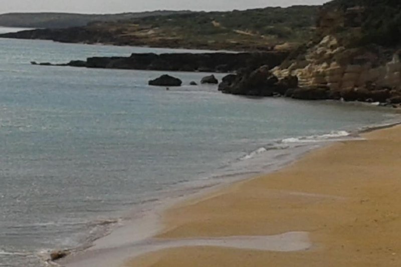 Una costa rocciosa con un mare calmo e una spiaggia di sabbia bianca.