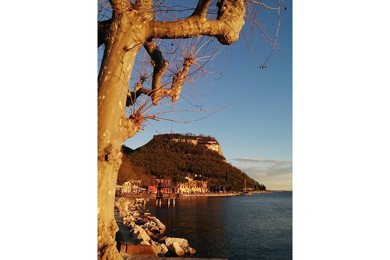 Garda im Winter. Eine ruhige Landschaft mit einem See, Bergen und einem atemberaubenden Sonnenuntergang.