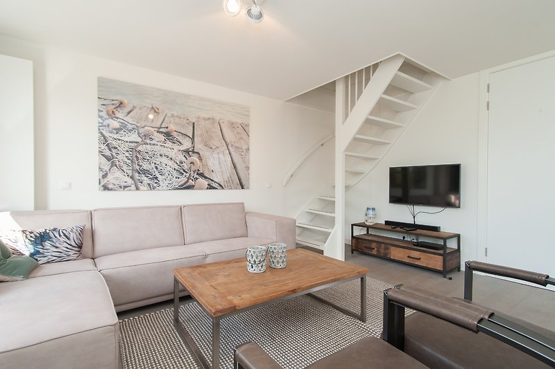 Wohnzimmer mit grauem Sofa, Tisch, Bilderrahmen und Holzboden.