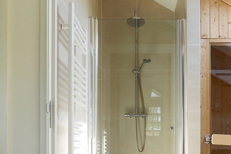 Modernes Badezimmer mit Dusche, Glaswand und Metallarmaturen.