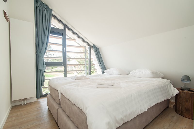 Schlafzimmer mit Holzbett, Fenster, Decke und Bettwäsche.