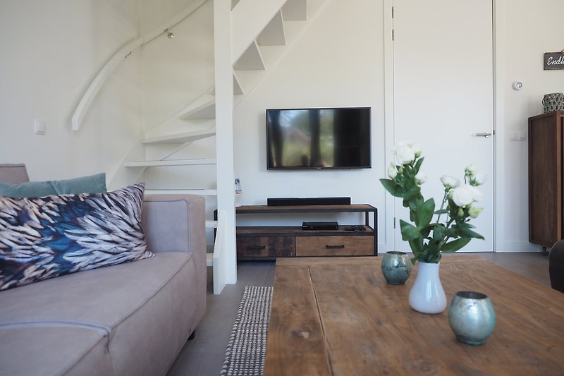 Wohnzimmer mit bequemer Couch, Pflanze, Holz und Fernseher.