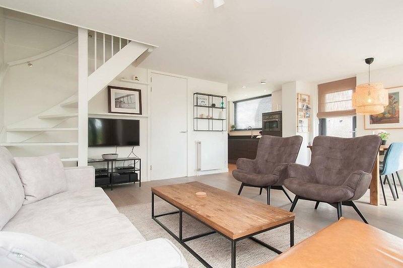 Wohnzimmer mit grauem Sofa, Tisch, Bilderrahmen und Holzdecke.