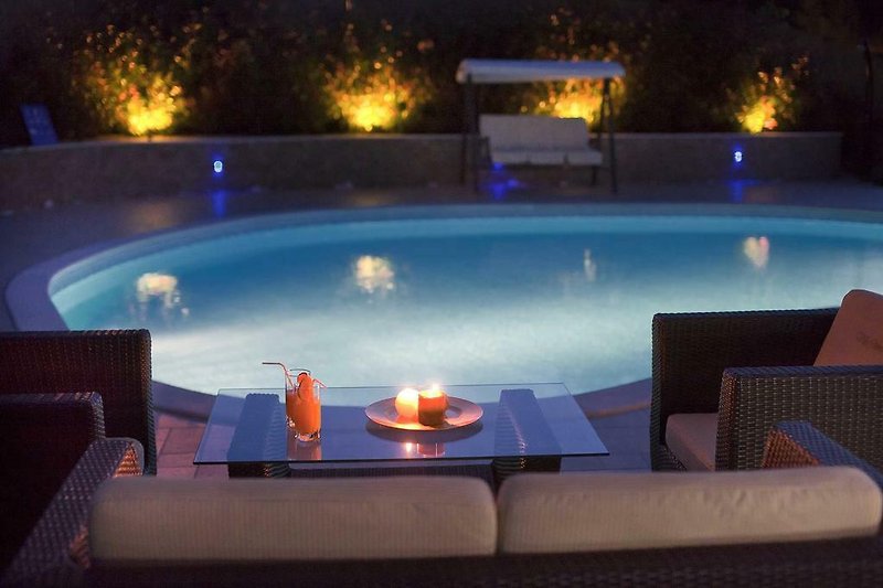Una vista notturna di un lussuoso resort con piscina illuminata e arredamento elegante.