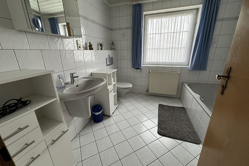Badezimmer 1 mit Spiegel, Waschbecken, Fenster und Badewanne.
