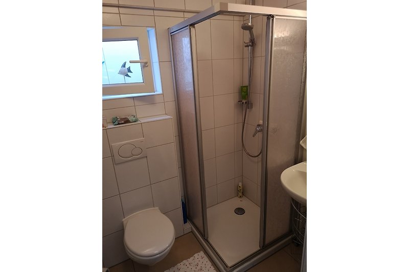 Schönes Badezimmer mit Toilette, Dusche mit Glasduschtür, Waschbecken und Spiegel, Elektroheizlüfter