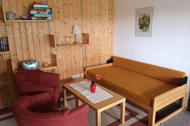 Gemütliches Wohnzimmer mit Holzmöbeln, Sesseln und Couch.