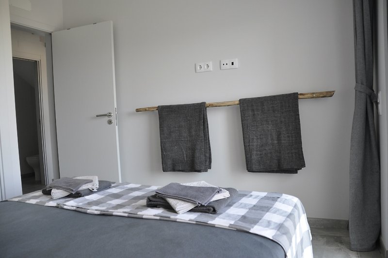 Gemütliches Schlafzimmer mit grauen Vorhängen und gemusterten Kissen.