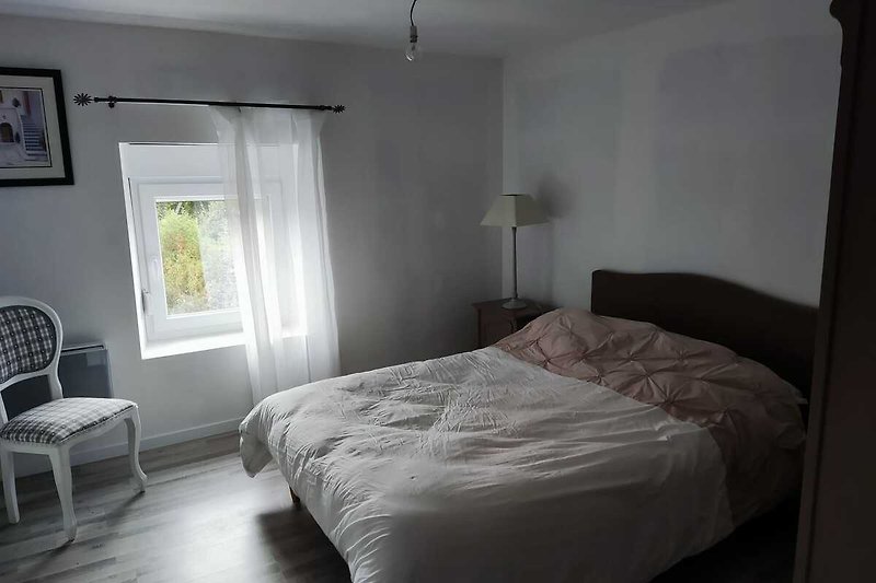 Gemütliches Schlafzimmer mit Bett, Kissen, Fenster und Lampen.