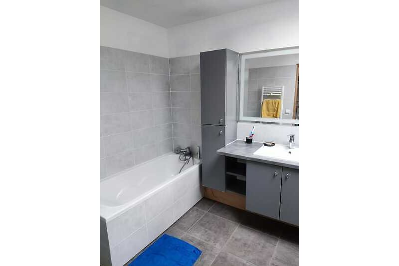 Badezimmer mit grauem Waschbecken, Spiegel und Badewanne.