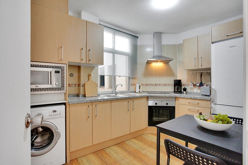 Moderne Küche mit Holz- und Edelstahlelementen, großem Fenster und modernen Geräten.