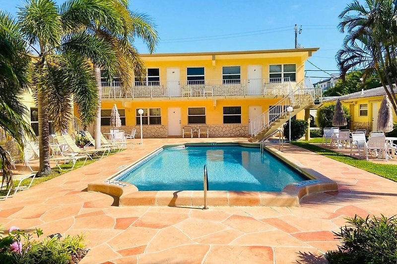 Ferienhaus mit Pool, Palmen und tropischer Landschaft.