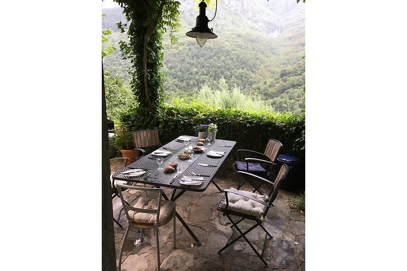 Charming outdoor setting with wooden furniture, lush greenery, and mountain views.