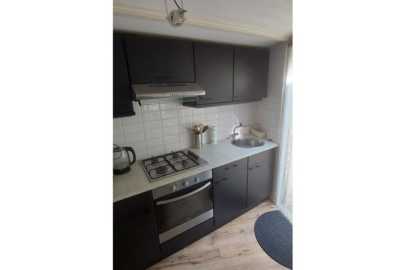 Moderne keuken met zwarte kasten, koffiezet apparaat, gasplaat, elektrische oven, afwasbak.