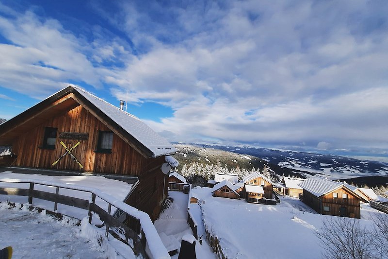 Blick auf verschneite Berge und Holzhütte in den Alpen.