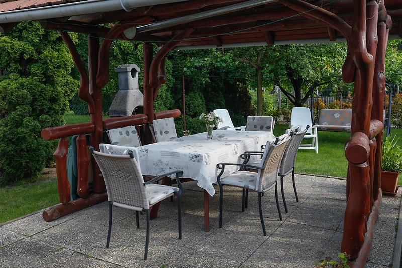 Garden rest. Outdoor dining area with wooden table, chairs, and shade. Enjoy leisure time surrounded by greenery.