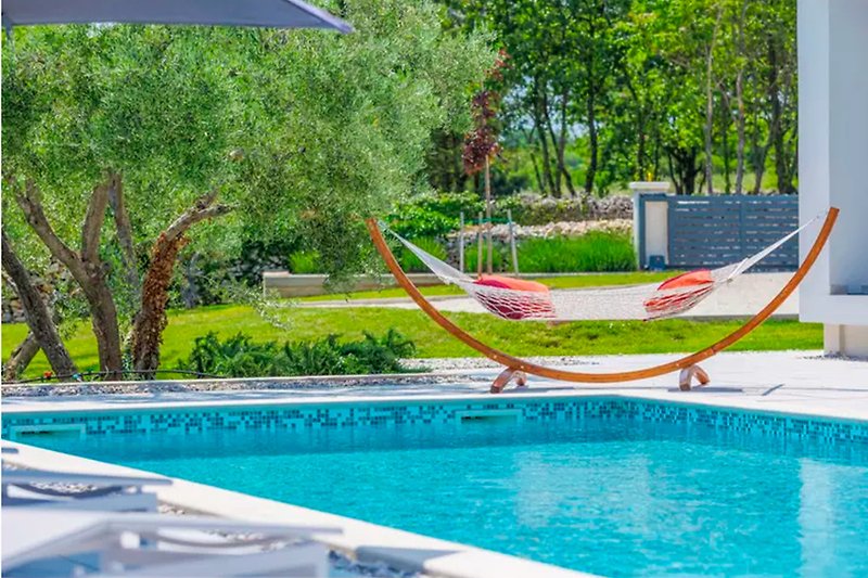 Relax by the pool with lush greenery and outdoor furniture.