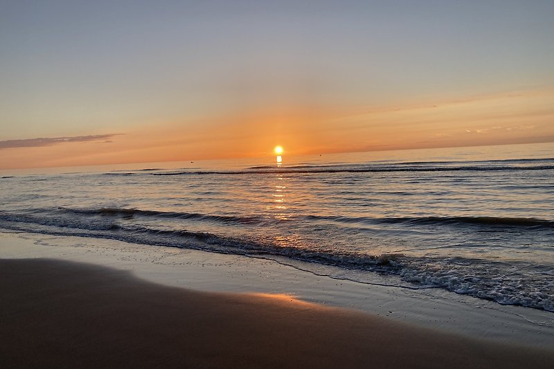 Traumhafter Sonnenuntergang über dem Meer mit rotem Himmel und ruhigen Wellen.