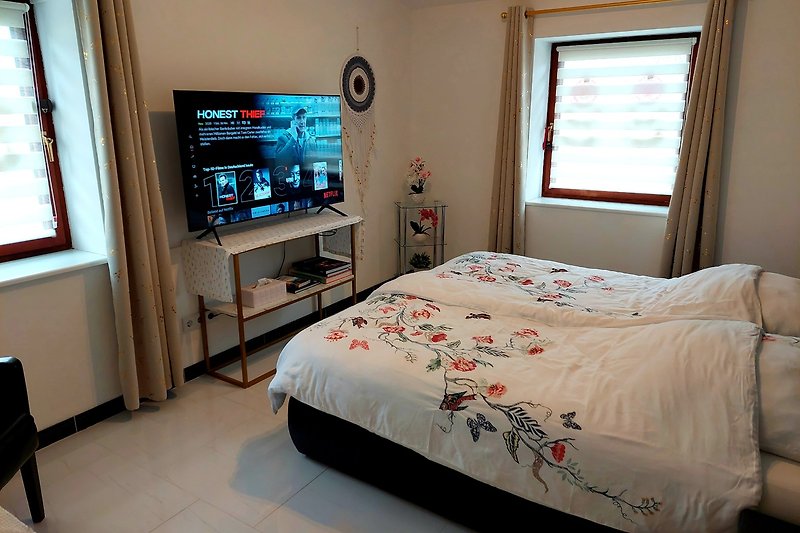Modernes Schlafzimmer mit Fernseher und gemütlichem Bett.
