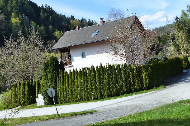 Ländliches Haus mit grünem Garten, blauem Himmel und Berglandschaft.