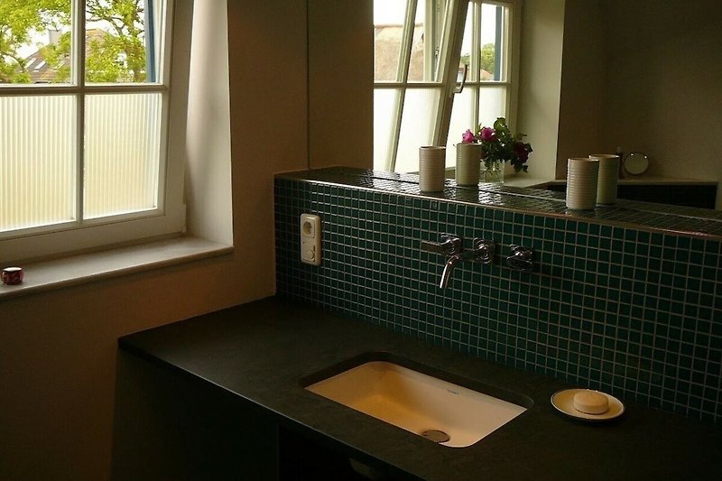 Badezimmer mit Spiegel, Waschbecken, Fenster und Pflanze.