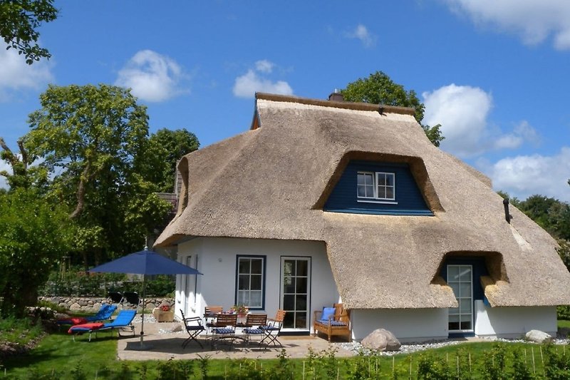 Thatched cottage with chairs under blue sky.