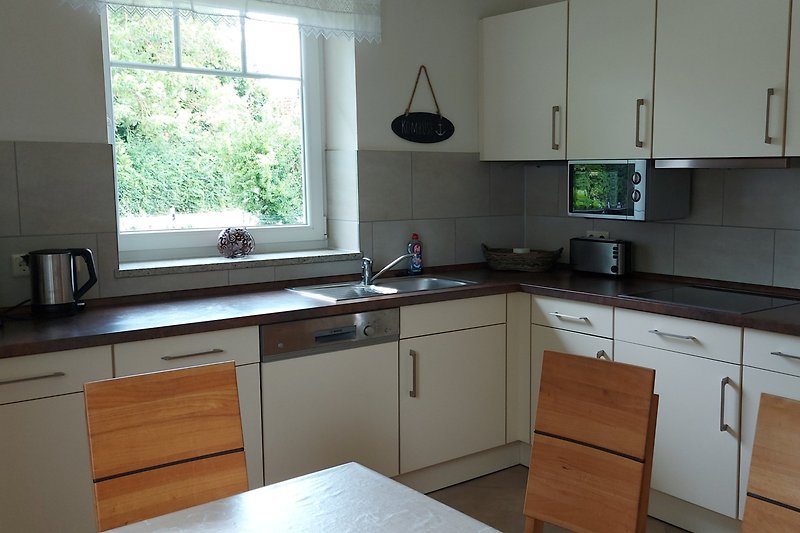 Moderne Küche mit weißen Schränken, Holzarbeitsplatte und Fenster.