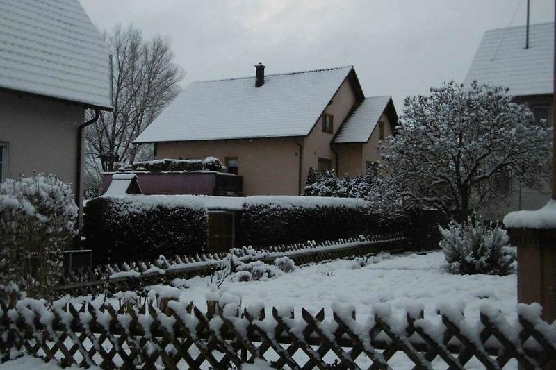 Winterlandschaft mit Haus, Garten und Schnee.