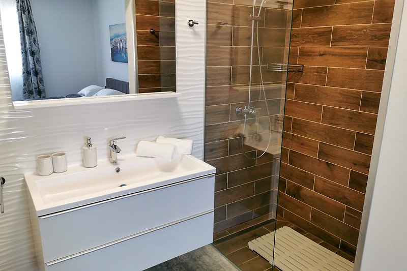 Elegantna kupaonica s modernim umivaonikom i staklenim tušem.