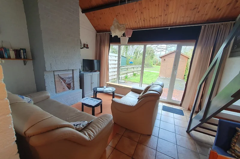 Wohnraum mit Sofa und Blick auf die Terrasse und Liegewiese.