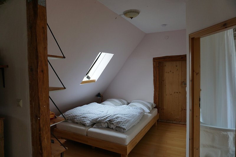 Gemütliches Schlafzimmer mit Holzbalken, Bett und Fenster.