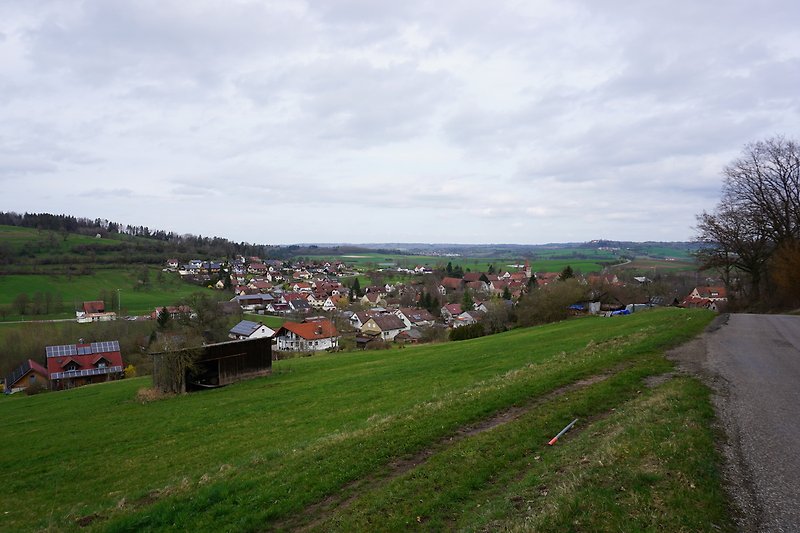 Landschaft mit Haus, Wiese, Hügel und Dorf.