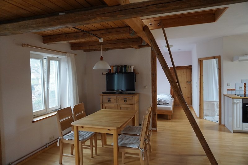 Geräumiges Wohnzimmer mit Holzbalken, Tisch, Couch und Pflanze.