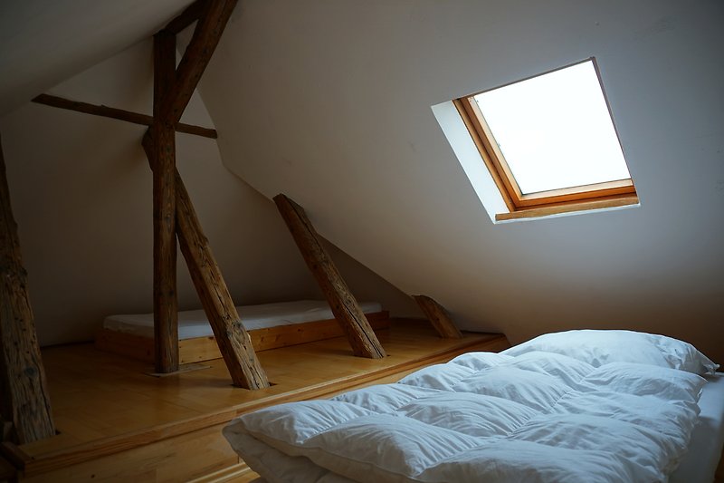 Schlafzimmer mit Holzbalken, Bett und Fenster - gemütliche Atmosphäre.