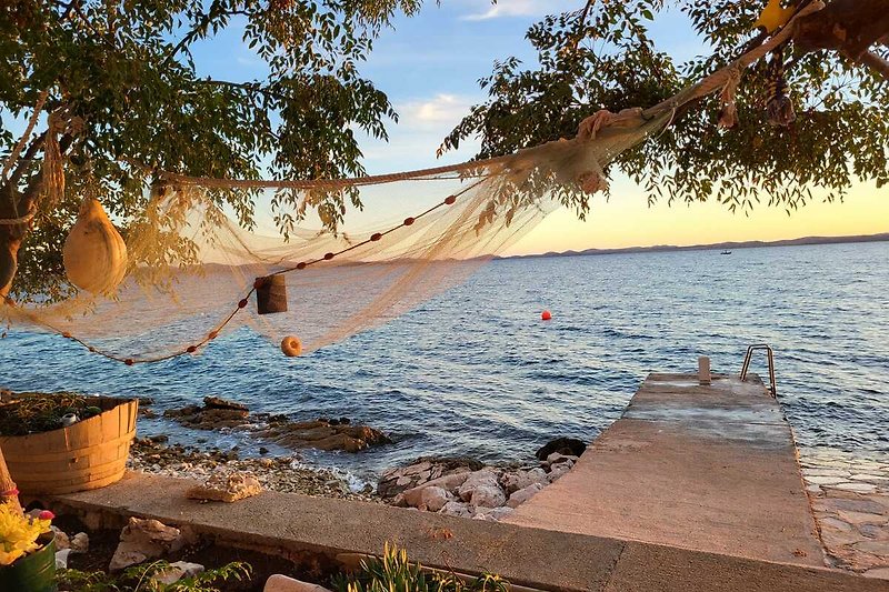 Privates Ferienhaus am See mit Strand, Palmen und Sonnenuntergang.