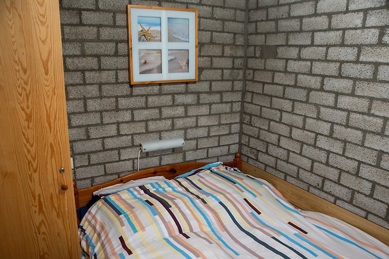 Schlafzimmer mit Holzdecke, Backsteinwand und Bettwäsche.